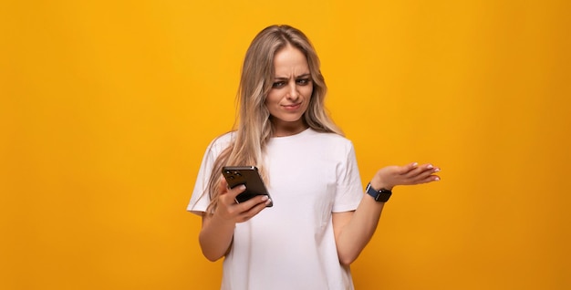 Indignant girl holding a smartphone in her hands on a yellow background