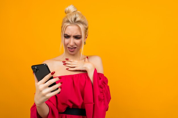 indignant girl in a red dress with a phone in her hands on a yellow surface with copy space