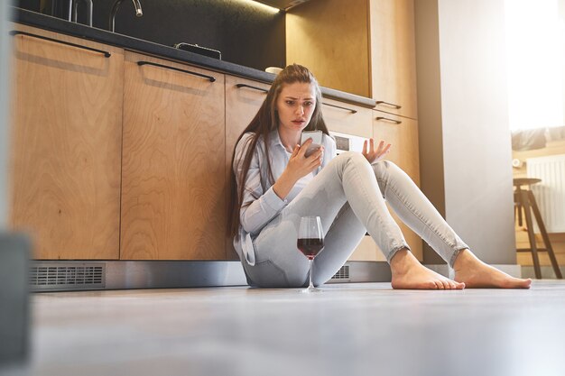 Indignant young Caucasian female with long hair staring at the cellular phone in her hand