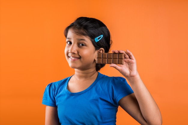 Indisch klein meisje dat chocoladeplak eet, geïsoleerd over oranje background