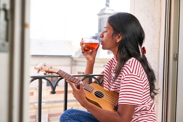 Indische vrouw die ukelele speelt op de vensterbank en een kopje thee drinkt