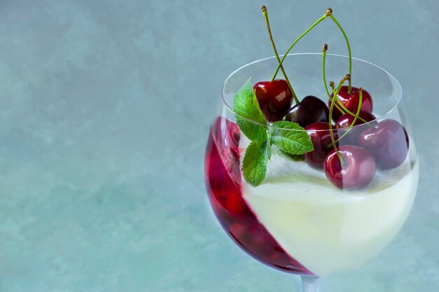 Foto dessert individuale in bicchiere di vino con ciliegia. panna cotta con frutti di bosco in vetro su grigio.