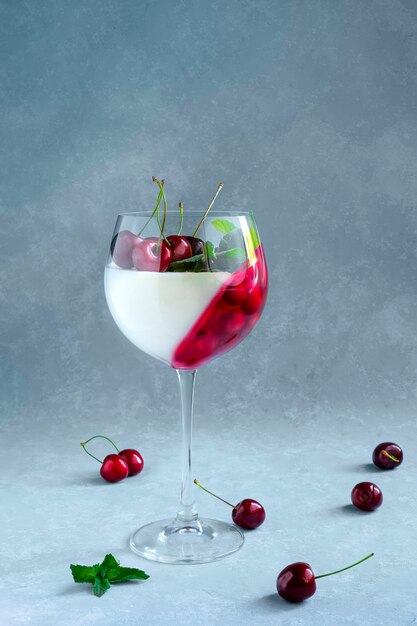 Individual dessert in wine glass with cherry. Panna cotta with berries in glass on grey.