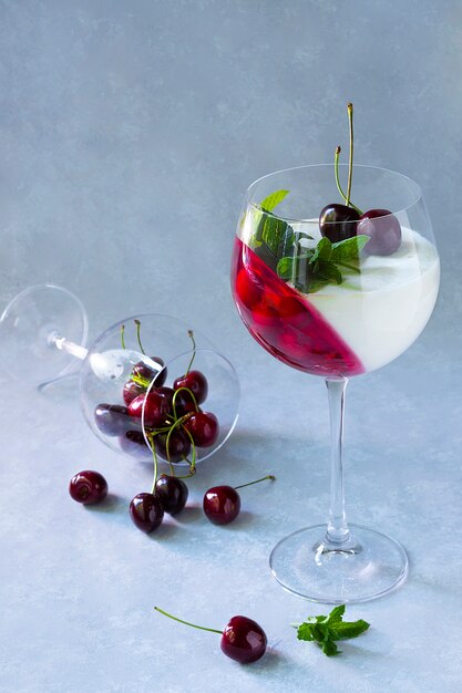 Individual dessert in wine glass with cherry. Panna cotta with berries in glass on grey.