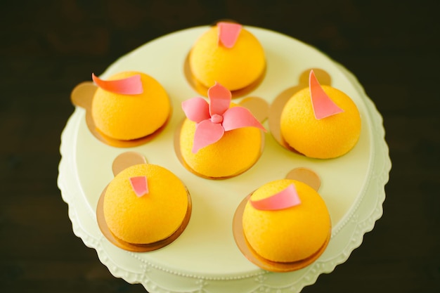 Individual yellow mousse cakes decorated with glazed flowers on an icing turntable