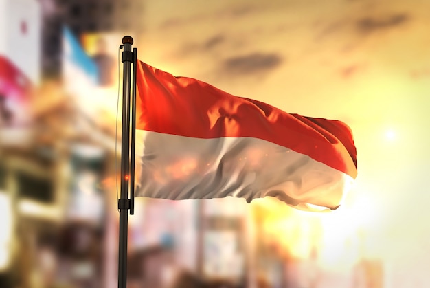 Bandiera dell'indonesia contro la città sfocata di sfondo all'illuminazione di alba