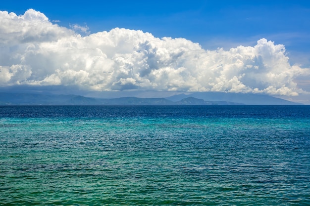 Индонезия. Солнечный день. Бирюзовая вода спокойного океана. Удивительно красивые облака над далеким островом