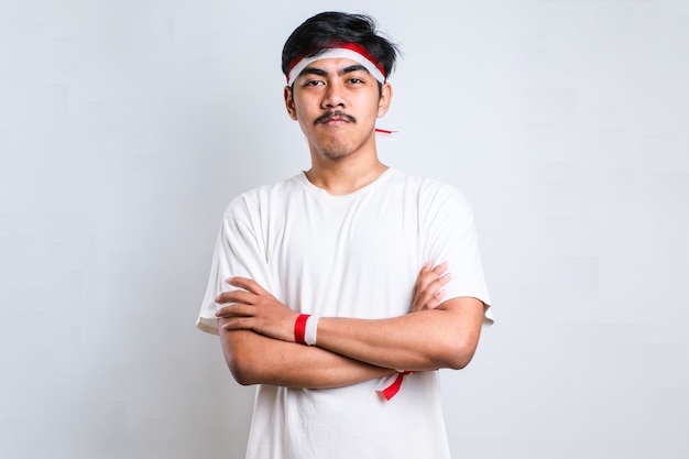 Indonesian boy doung crossed arms wearing red and white head band. Looking at the camera. positive person.