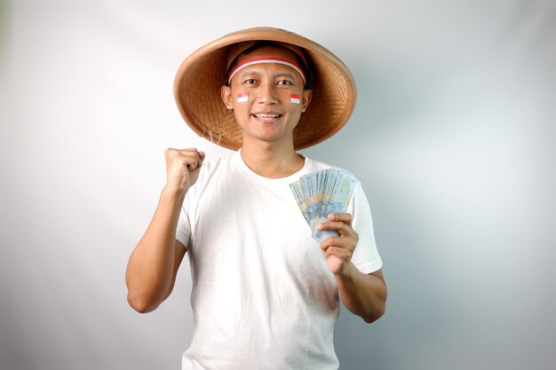 Photo indonesian farmer clenched fist while holding paper money and showing happy expression