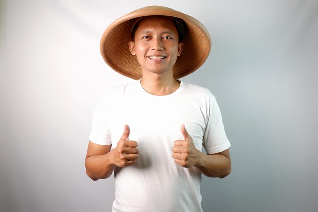 Indonesian farmer wearing conical hat showing happy expression while giving two thumb up