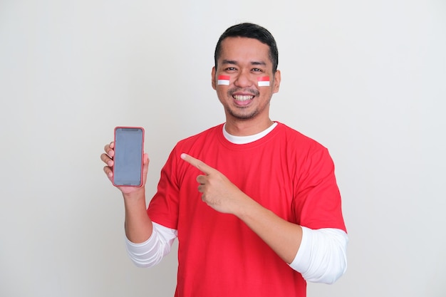 Индонезийский мужчина указывает на пустой экран мобильного телефона, который он держит со счастливым выражением лица