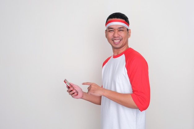 Indonesian man smiling while pointing to mobile phone that he hold