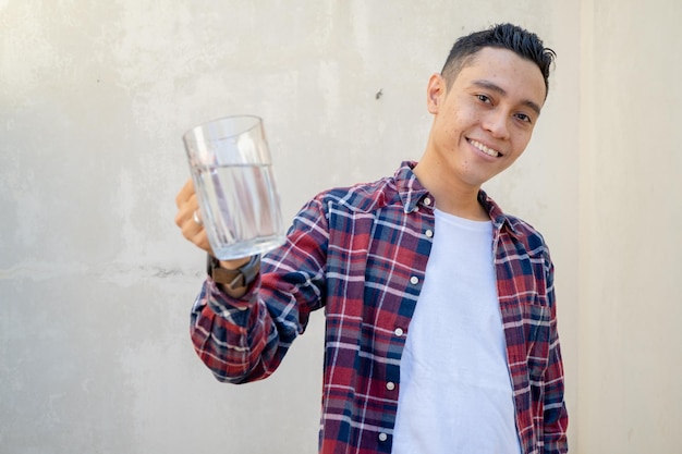 Indonesian man wear casual clothes hold a glass water and drink water