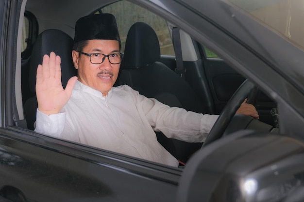 Photo indonesian moslem man waving his hand to say good bye from inside car cabin