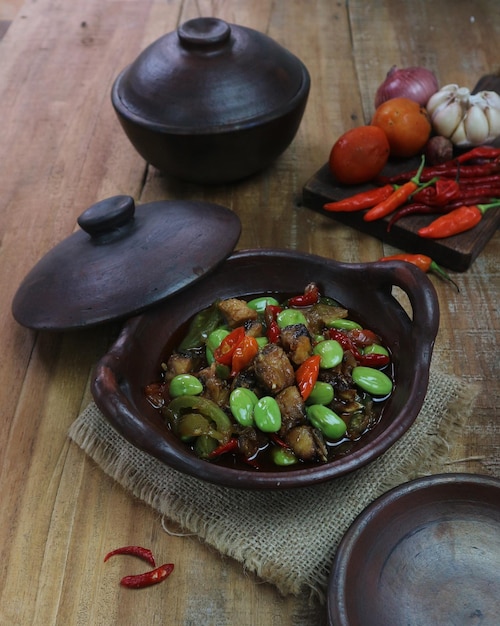 Photo indonesian spicy homemade stirfried petai served in a clay pan with spices as a background