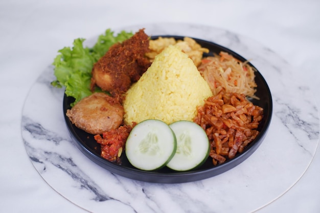 indonesian style yellow rice with chicken and side dishes in black plate