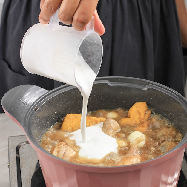 Indonesian/Thai Home Cooking Process, Female Hand Pour Coconut Milk in to the Pan, Making Indonesian/Thai Style Curry, Traditional Asian Gourmet Called Opor Ayam, Gulai, Kari, or Kare