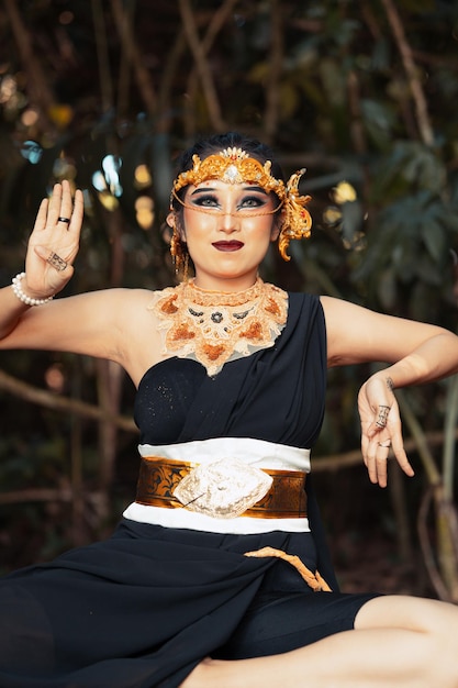황금 왕관과 황금 목걸이를 착용하고 검은 댄스 의상을 입고 바위에 앉아 있는 인도네시아 여성