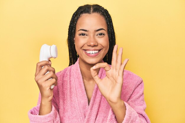 Foto donna indonesiana con detergente per il viso su giallo allegro e fiducioso che mostra un gesto ok