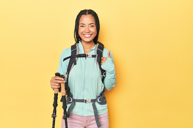 Indonesian woman with hiking gear on yellow smiling and raising thumb up