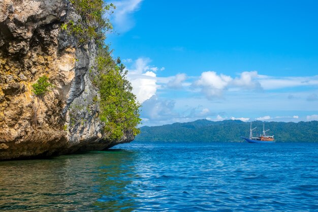 Indonesië. Rotsachtige kust van een tropisch eiland bij zonnig weer. Regenwoud op een helling. Jacht in de verte