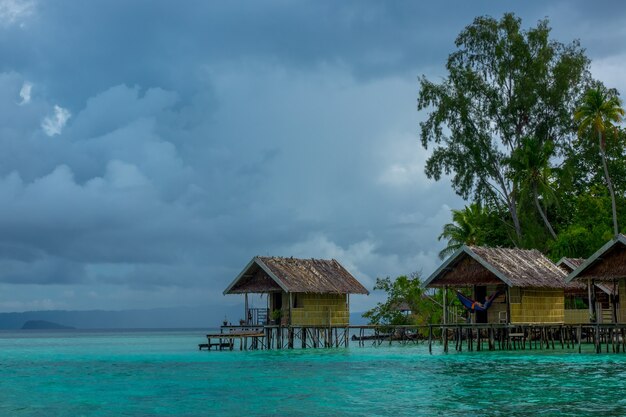 Indonesische eilanden. Bewolkte avond. Kust van de oceaan en de jungle. Hutten op palen in het water