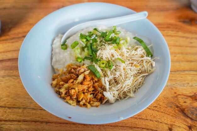 Indonesische Kippenpap Indonesisch traditioneel eten Bestaat uit pap gemengd met kippenvlees geserveerd met eiergroenten en crackers op blauw bord geïsoleerd op witte achtergrond