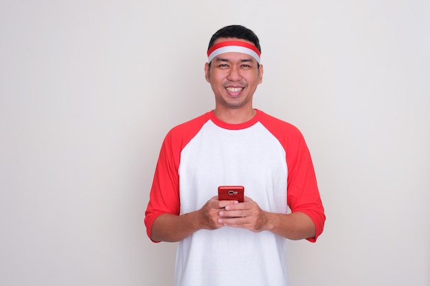 Indonesische man die gelukkig glimlacht terwijl hij een mobiele telefoon vasthoudt
