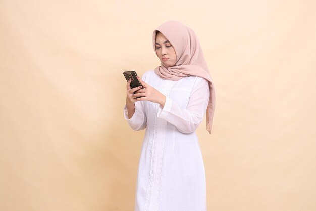 Foto indonesische moslimvrouw met een hijab fronst en bedient een mobiele gadget met beide handen lifestyle
