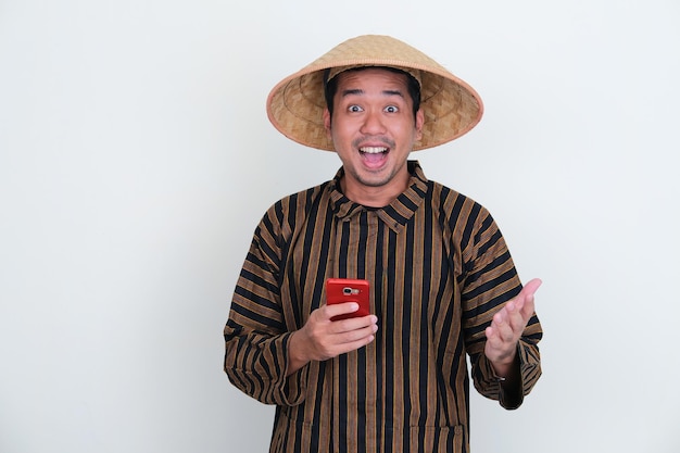 Indonesische traditionele boer die opgewonden uitdrukking toont terwijl hij mobiele telefoon vasthoudt