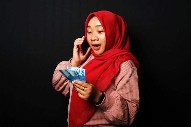 Indonesische vrouw kreeg een telefoontje en hield veel geld vast met een gelukkige uitdrukking geïsoleerd op zwarte achtergrond