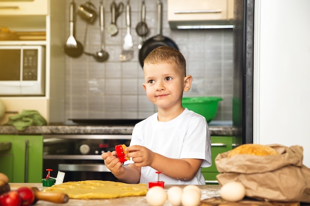 Indoor activiteit. Jonge positieve kind jongen koken in de keuken. Maak koekjes