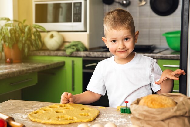 Indoor activiteit. Jonge positieve kind jongen koken in de keuken. Maak koekjes