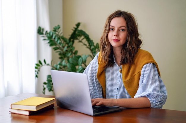 Indoor home office portrait of trendy blogge influencer working on her laptop, stylish clothes, minimalistic interior.