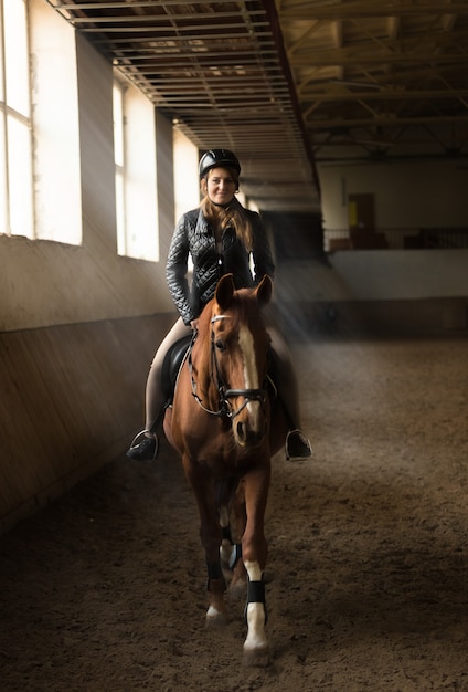 Indoor photo of young woman jockey riding horse on manege