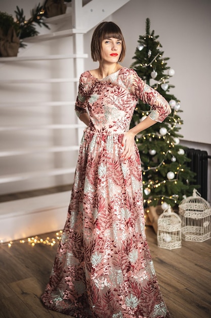 Indoor portrait of confident girl in a long dress posing near christmas tree.Soft focus. Selective focus.