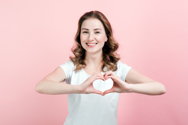 Indoor portrait of excited curly woman makes a gesture a heart with her fingers.