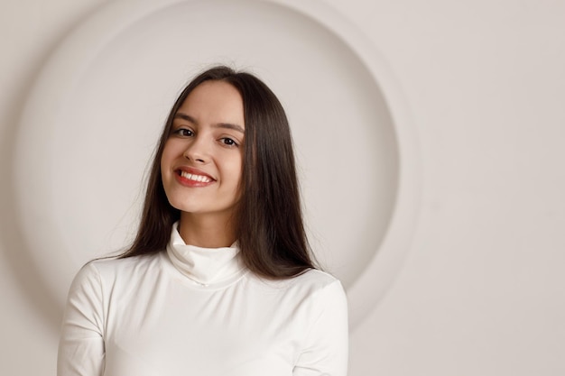 원형 복사 공간이 있는 흰색 배경에 있는 긍정적인 웃는 브루네트 젊은 여성의 실내 초상화