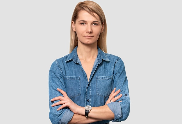 Indoor portrait of serious Caucasian female freelancer pleasant appearance with blonde hair dressed in blue denim shirt works distantly at home Business woman posing on white studio wall