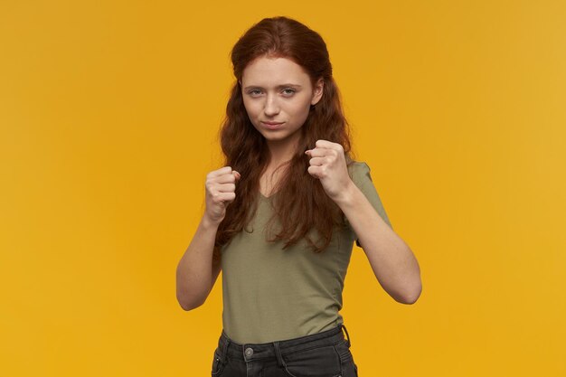 Indoor portrait of young ginger female ready to fight for her rights.. isolated over yellow background