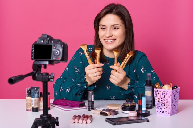 Indoor shot of caucasian woman showing cosmetic powder brush isolated over pink