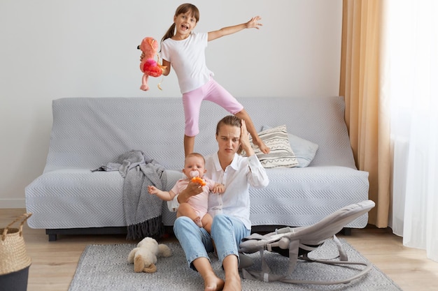 Indoor shot of mother in depression by screaming children problems of motherhood sitting on floor and suffering headache dont know what to do with kids