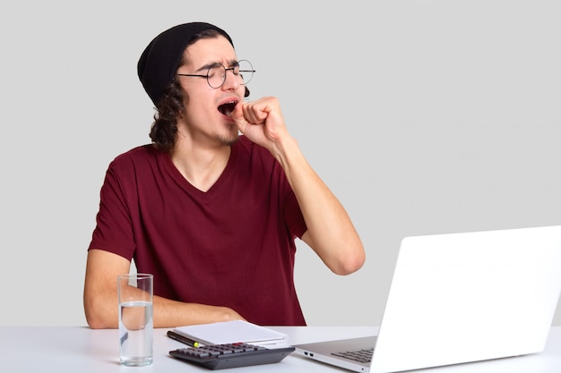 Indoor shot of overworked man yawns as needs rest