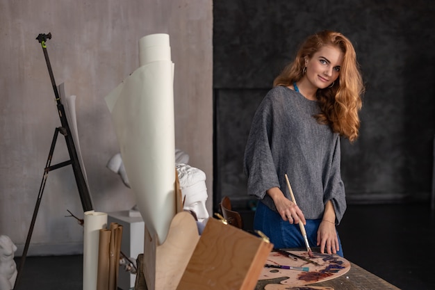 Indoor shot of professional female artist painting on canvas in studio.