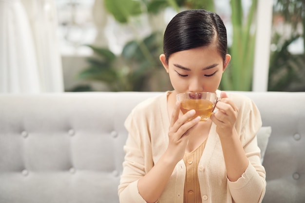 차를 마시는 웃는 아시아 여성의 실내 샷.