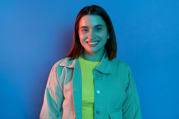 Indoor shot of smiling happy satisfied woman wearing stylish jacket posing isolated on neon light background looking at camera expressing positive expression