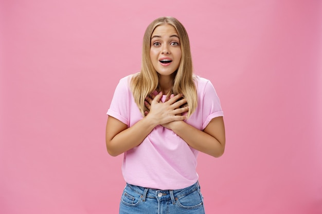 Indoor shot of touched surprised good-looking nice girl in t-shirt and jeans holding palms on heart gasping from amusement and amazement reacting to awesome pleasant news grateful and happy