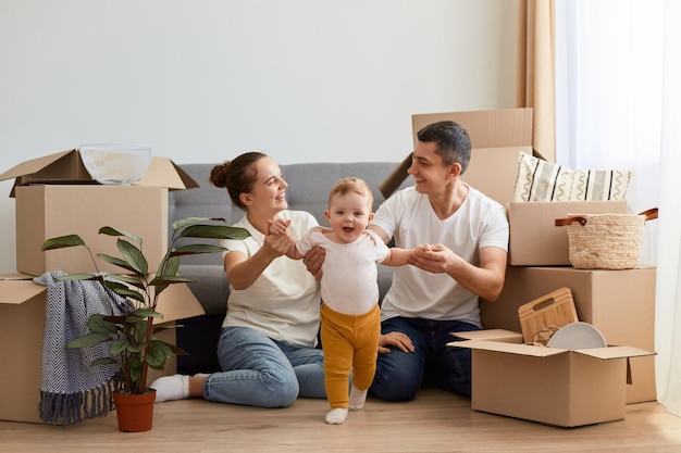 Indoor shot of wife and husband posing in their new apartment on moving day family with baby relocating in a new house and feels happy playing with kid happily