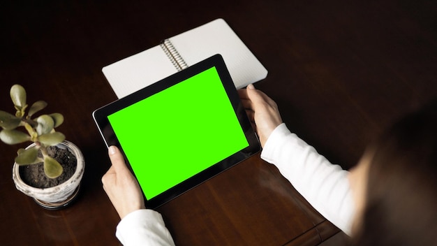 女性の屋内ショットは、暗い木製のテーブルに緑色の画面でタブレットPCを保持します。