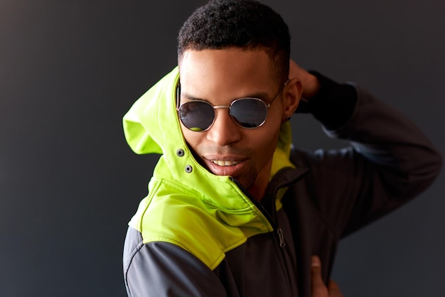 Indoor shot of young African American man wearing round mirror sunglasses touching his head with serious expression looking down posing over black studio background Thoughtful male thinking